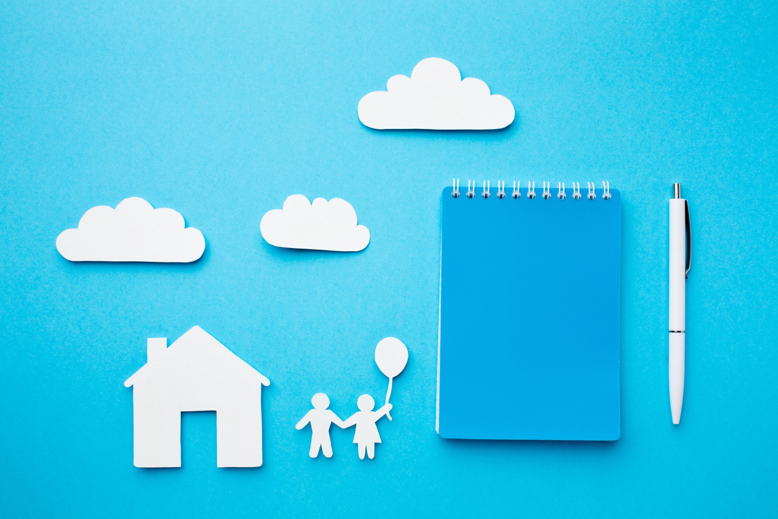 Cut outs of a house, two people with one holding a balloon and clouds on a blue background